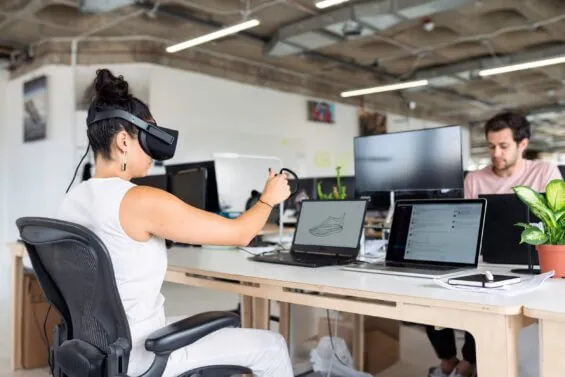 A woman uses a virtual reality headset while sitting at her desk in an office.