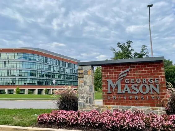 The entrance sign to George Mason University's main campus in Fairfax,Virginia with a large glass building in the background.