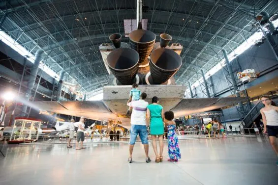 A young family observes a large jet plane in a museum.