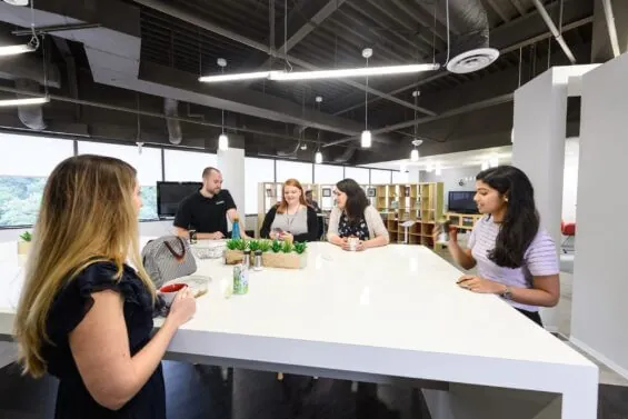 A group of coworkers stand around a table together.