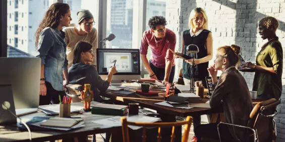 A group of young professionals brainstorm around a table together in a contemporary office space.