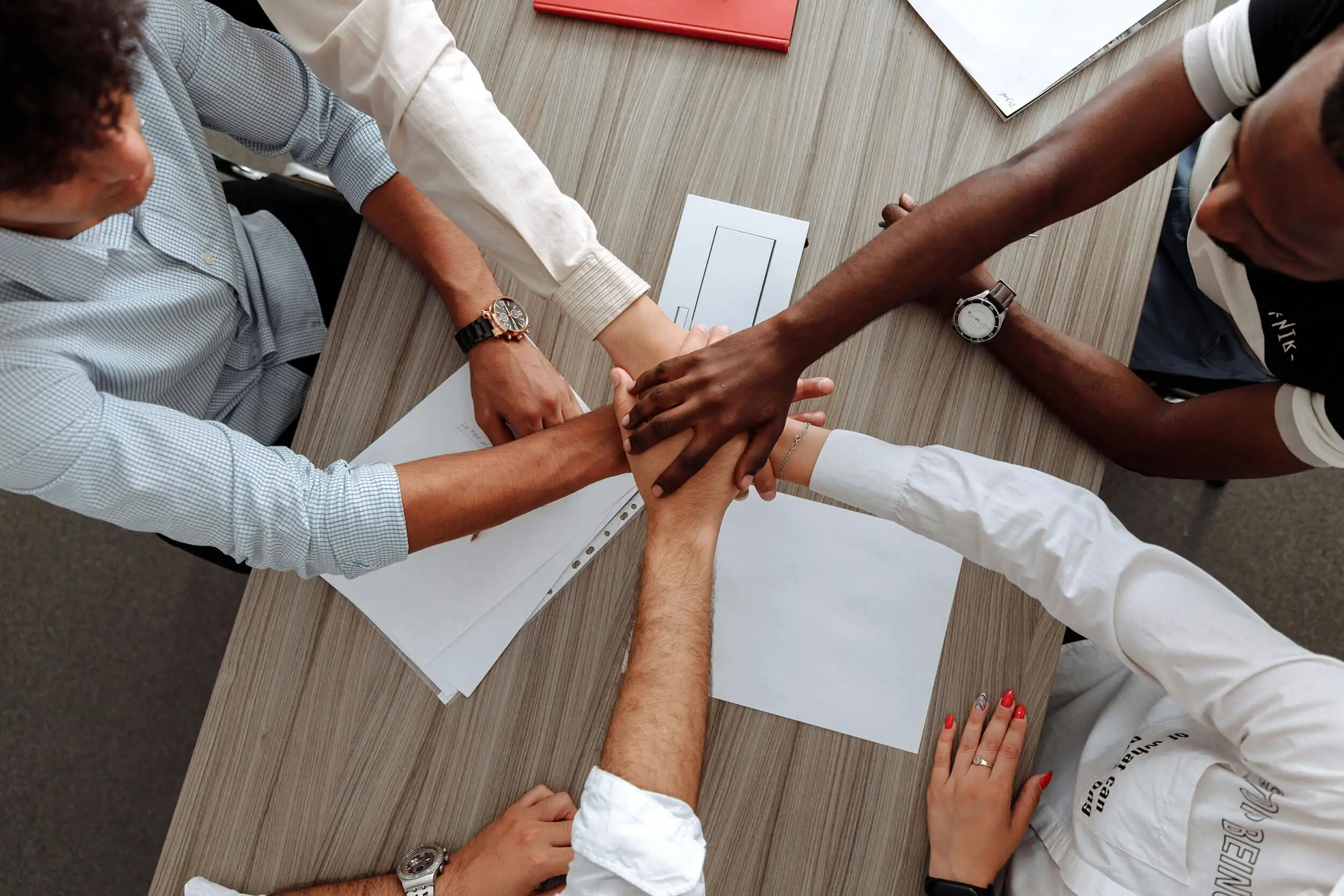 A team of people at a table puts their hands together in the middle.