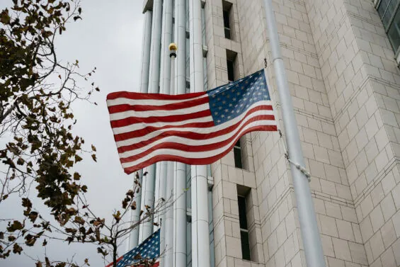 The American flag waves in the wind outside of a building.