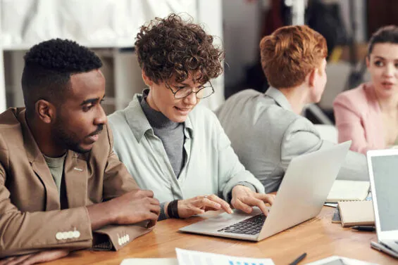 Two young people work together on a laptop at a table.