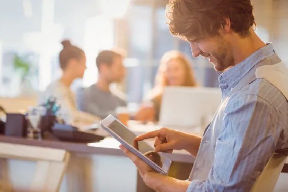 A smiling young man uses a digital tablet at an office.