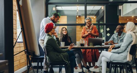 A diverse group of business people smile as they collaborate around a table in a modern office.