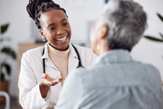 A smiling young doctor speaks to an older patient.