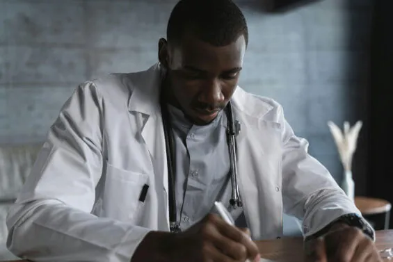 A doctor sits at a desk to write.