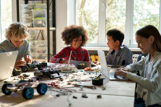 A group of diverse school children interact with gadgets in an elementary robotics class.