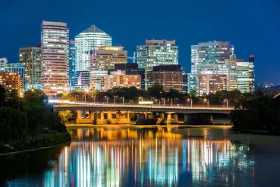 At dusk, brightly lit buildings in Arlington rise behind a bridge going over a river.