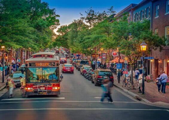 A trolley goes down a bustling street in the summer in Alexandria, Virginia.