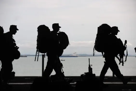 Silhoutted soldiers walk in a line with the ocean visible behind them.